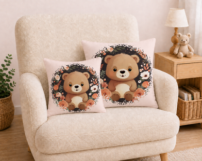 „Hellbeiges Kuschelkissen aus Baumwolle mit einem sitzenden braunen Teddybären in der Mitte, umgeben von einem kreisförmigen Kranz aus dunklen Zweigen und Blüten in Creme-, Beige- und Apricottönen.“