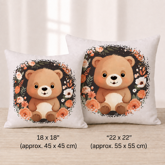 „Hellbeiges Kuschelkissen aus Baumwolle mit einem sitzenden braunen Teddybären in der Mitte, umgeben von einem kreisförmigen Kranz aus dunklen Zweigen und Blüten in Creme-, Beige- und Apricottönen.“