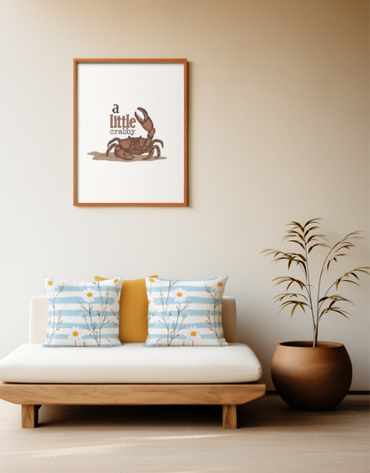 Zwei quadratische Baumwoll Kissen mit Gänseblümchen-Muster platziert auf einem Sofa im Japandi Stil. Das Design zeigt filigrane, grüne Stängel mit weißen Gänseblümchen und kleinen, gelb-orangefarbenen Knospen. Der Hintergrund besteht aus horizontal verlaufenden Streifen in Hellblau mit einer leichten Pinselstruktur und Weiß.