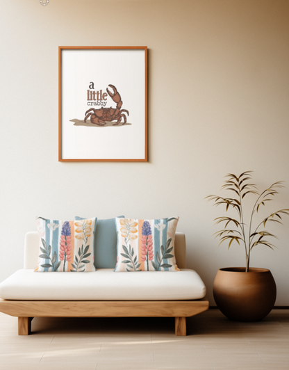 Zwei quadratische Baumwoll Kissen mit einem floralen Lupinen-Muster platziert auf einem Sofa im Japandi Stil. Im Zentrum steht eine detailreiche Lupine mit rosa und blau-violetten Blüten, umgeben von Zweigen mit dunkelgrünen sowie gelb-orangefarbenen Blättern. Der Hintergrund ist mit vertikalen Aquarell-Streifen in Blau-Grau, softem Orange und Weiß gestaltet.
