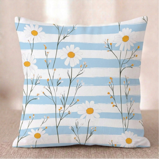 Ein quadratischer Baumwoll - Kissen-bezug mit Gänseblümchen-Muster vor einem hellen Hintergrund. Das Design zeigt filigrane, grüne Stängel mit weißen Gänseblümchen und kleinen, gelb-orangefarbenen Knospen. Der Hintergrund besteht aus horizontal verlaufenden Streifen in Hellblau mit einer leichten Pinselstruktur und Weiß.