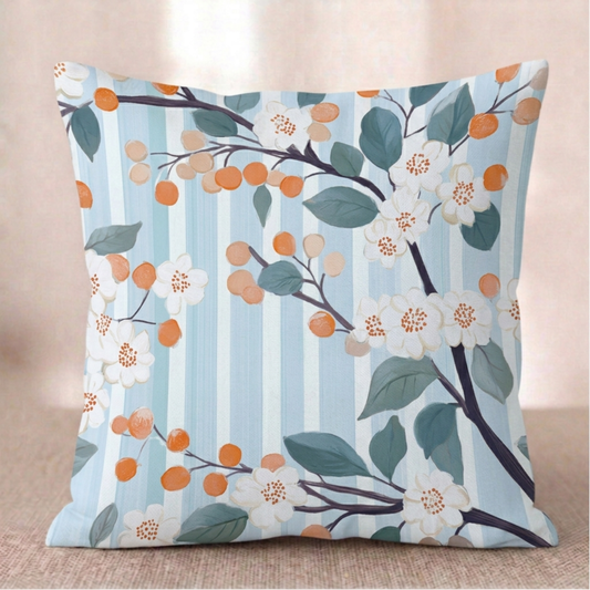 Ein quadratischer Baumwoll - Kissen-bezug mit Orangenblüten-Muster vor einem hellen Hintergrund. Das Design zeigt dunkle Zweige mit kleinen weißen Orangenblüten, graublauen Blättern und runden, orangefarbenen Früchten. Der Hintergrund besteht aus feinen, vertikalen Streifen in Hellblau und Weiß mit einer leichten Textur.
