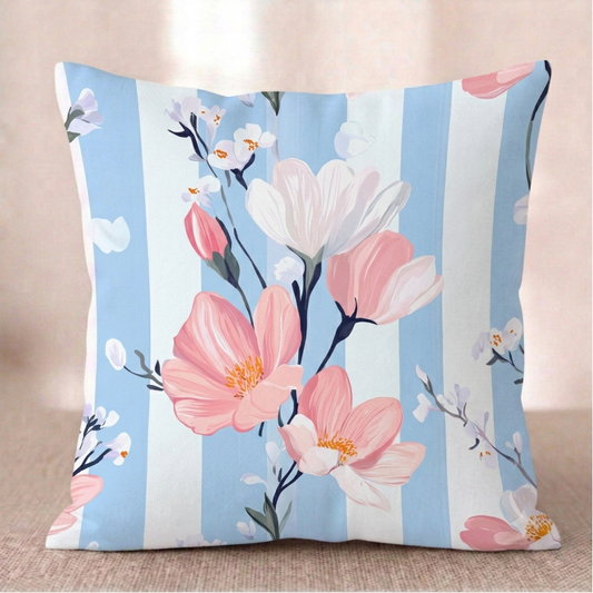 Ein quadratischer Baumwoll - Kissen-bezug mit Magnolien-Muster vor einem hellen Hintergrund. Das Design zeigt Zweige mit großen rosa und weißen Magnolienblüten sowie kleine, zarte weiße Blütenknospen. Der Hintergrund besteht aus breiten, vertikalen Streifen in Hellblau mit einer feinen Holz- oder Aquarelltextur und Weiß.