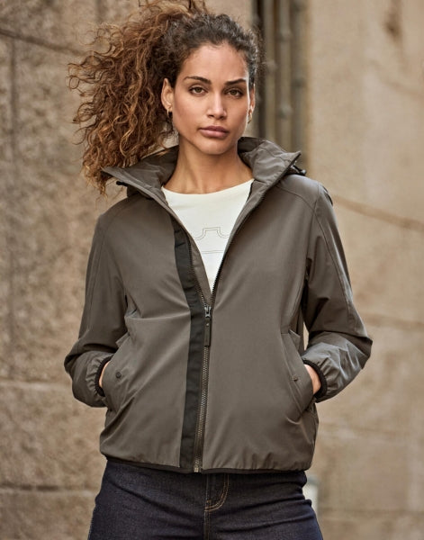 Damen Adventure Jacke in Dark Olive mit glatter Oberfläche und leicht taillierter Passform. Mit Kapuze, hochschließendem Kragen, Frontreißverschluss und seitlichen Eingriff Taschen.