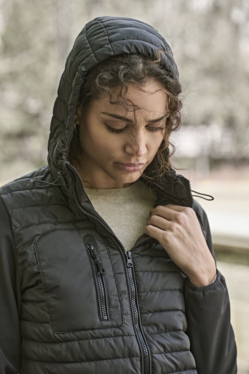 Damen Hooded Crossover Jacke in schwarz mit horizontal gesteppter Vorderseite und glatten Stretch-Ärmeln. Körpernah geschnitten mit Kapuze, hohem Kragen und durchgehendem Frontreißverschluss.