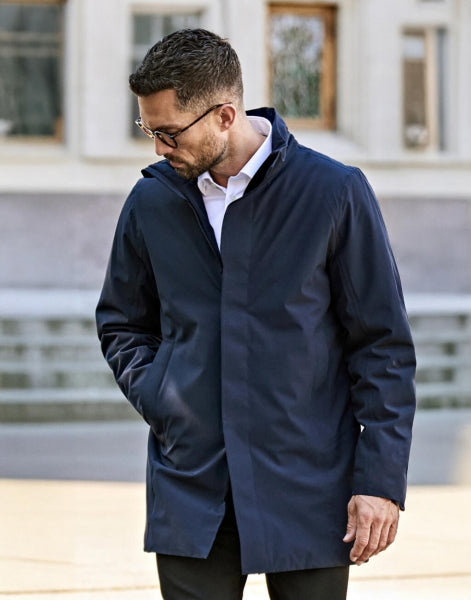 Ein Herren All Weather Parka in  Dunkelblau mit geradem, längerem Schnitt bis über die Hüfte. Schlichtes Design mit hochstehendem Kragen, verdecktem Frontreißverschluss und zwei seitlichen Reißverschlusstaschen.