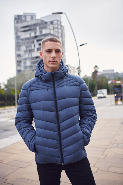 Eine Hüftlange Herrenjacke in Fog Blue mit Kapuze, hohem Kragen und langen Ärmeln. Die schmale Steppung verleiht der Jacke eine gleichmäßige Struktur und einen sportlichen Charakter