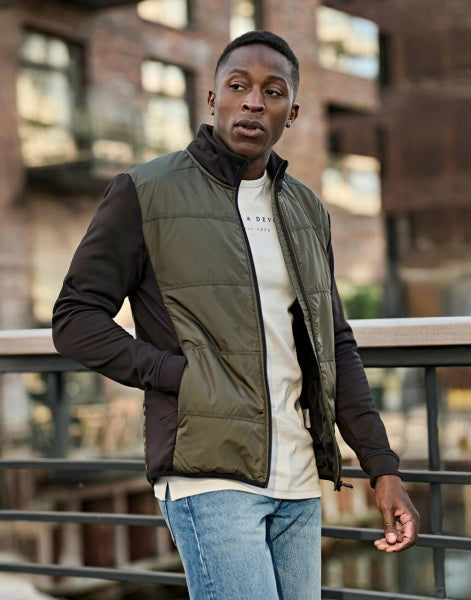 Herren Hybrid-Stretch-Jacke mit wattierter, quer gesteppter Vorderseite in Dunkelgrün, schwarzen Stretch-Ärmeln und seitlichen Einsätzen. Die Jacke ist körpernah geschnitten und hat einen hohen Stehkragen sowie einen durchgehenden Front Reißverschluss.