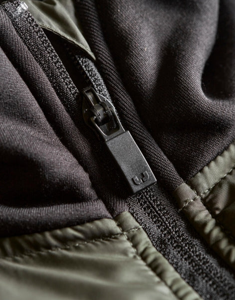 Herren Hybrid-Stretch-Jacke mit wattierter, quer gesteppter Vorderseite in Dunkelgrün, schwarzen Stretch-Ärmeln und seitlichen Einsätzen. Die Jacke ist körpernah geschnitten und hat einen hohen Stehkragen sowie einen durchgehenden Front Reißverschluss.