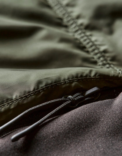 Herren Hybrid-Stretch-Weste mit wattierter, quer gesteppter Vorderseite in tiefen grün und seitlichen Einsätzen. Die Weste ist körpernah geschnitten und hat einen hohen Stehkragen sowie einen durchgehenden Front Reißverschluss.