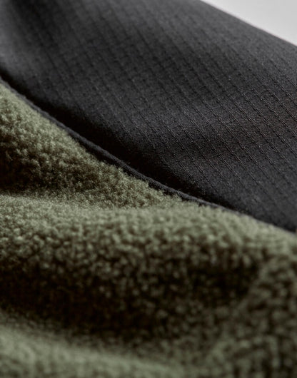 Mountain Fleecejacke in Deep Green/Black mit schwarzem Reißverschluss und dunklen Kontrastbesätzen an Brust, Schultern und Ärmeln. Die hüftlange Jacke ist körpernah geschnitten, hat einen hohen Kragen und seitliche Reißverschlusstaschen.
