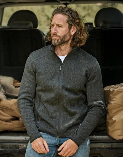 Mann trägt eine  Schwarze Outdoor Fleece Jacke in geradem, körpernahem Schnitt. Die hüftlange Fleecejacke hat einen hohen Stehkragen, lange Ärmel und zwei seitliche Reißverschlusstaschen. Das schlichte Design wird durch dezente schwarze Details an Reißverschlüssen und Abschlüssen ergänzt.
