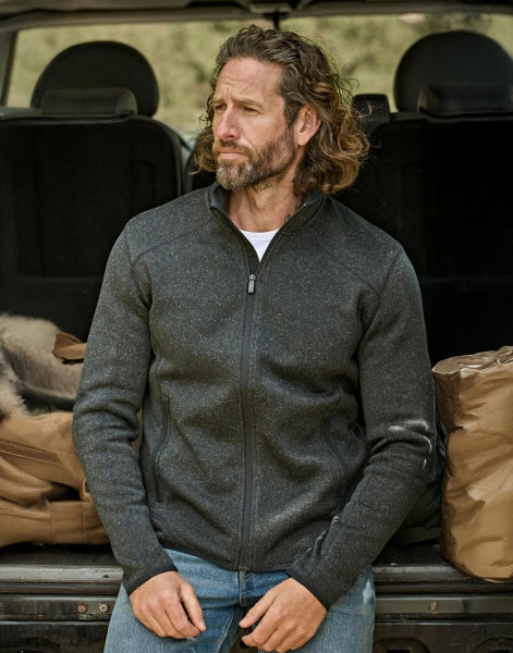 Mann trägt eine  Schwarze Outdoor Fleece Jacke in geradem, körpernahem Schnitt. Die hüftlange Fleecejacke hat einen hohen Stehkragen, lange Ärmel und zwei seitliche Reißverschlusstaschen. Das schlichte Design wird durch dezente schwarze Details an Reißverschlüssen und Abschlüssen ergänzt.
