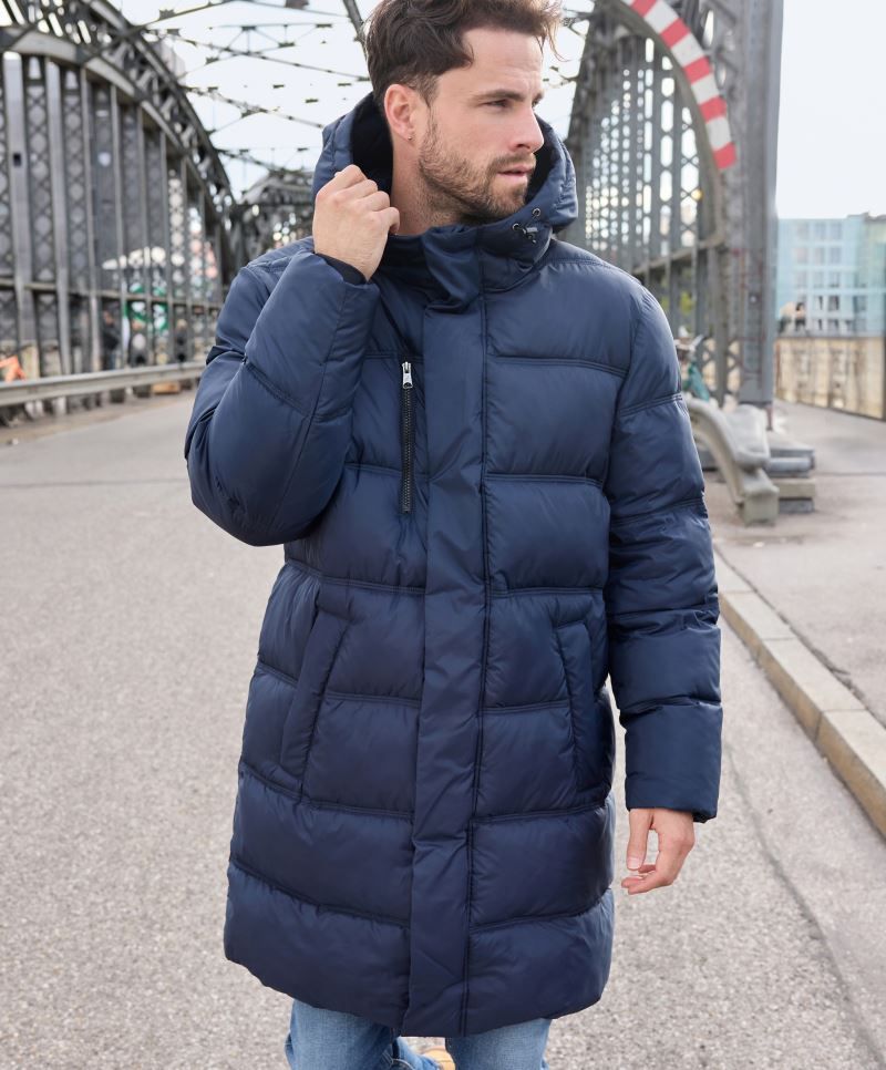 Herren Puffermantel in Dunkelblau mit gleichmäßiger horizontaler Steppung und voluminöser Wattierung. Knielanger Schnitt mit Kapuze, hochschließendem Kragen, durchgehendem Frontreißverschluss und seitlichen Eingriff Taschen.