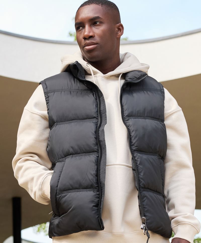 Herren Puffer Weste in schwarz mit gleichmäßiger horizontaler Steppung und voluminöser Wattierung. Hüftlanger Schnitt und hochschließendem Kragen, durchgehendem Frontreißverschluss und seitlichen Eingriff Taschen.