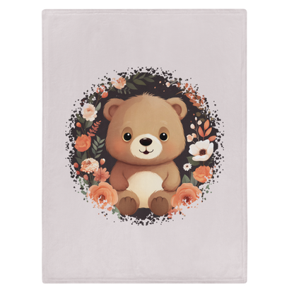 „Hellbeige Kuscheldecke mit einem sitzenden braunen Teddybären in der Mitte, umgeben von einem kreisförmigen Kranz aus dunklen Zweigen und Blüten in Creme-, Beige- und Apricottönen.“