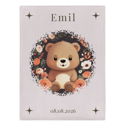 „Hellbeige Kuscheldecke mit einem sitzenden braunen Teddybären in der Mitte, umgeben von einem kreisförmigen Kranz aus dunklen Zweigen und Blüten in Creme-, Beige- und Apricottönen.“