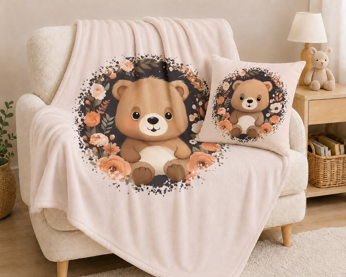 „Hellbeiges Kuschelkissen aus Baumwolle mit einem sitzenden braunen Teddybären in der Mitte, umgeben von einem kreisförmigen Kranz aus dunklen Zweigen und Blüten in Creme-, Beige- und Apricottönen.“