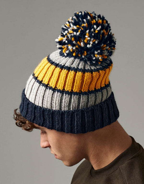 Unisex Strickmütze in dijon blue mit Bommel  mit drei unterschiedlichen Farben ( dunkelblau, gelb und weiß) mit breitem Umschlag und strukturiertem Strickmuster.