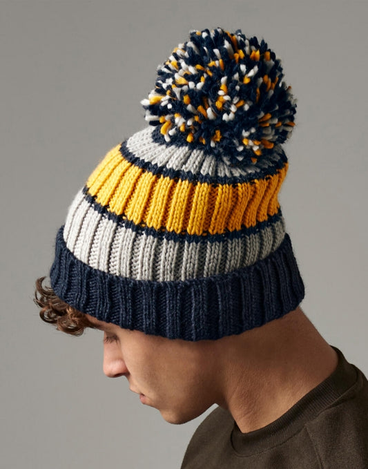 Unisex Strickmütze in dijon blue mit Bommel  mit drei unterschiedlichen Farben ( dunkelblau, gelb und weiß) mit breitem Umschlag und strukturiertem Strickmuster.