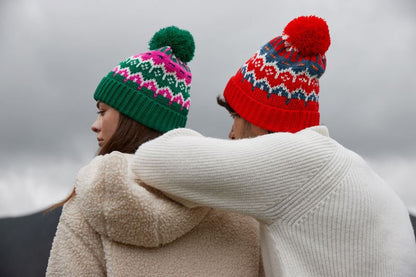 Unisex Strickmütze in Alpine Racer (Rot mit grau weißem Muster) und rotem Bommel  sowie einem breitem Umschlag mit strukturiertem Strickmuster.