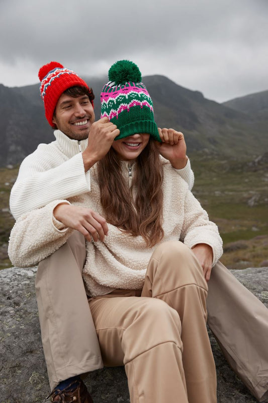 Unisex Strickmütze in Alpine Racer (Rot mit grau weißem Muster) und rotem Bommel  sowie einem breitem Umschlag mit strukturiertem Strickmuster.