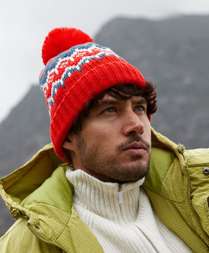 Unisex Strickmütze in Alpine Racer (Rot mit grau weißem Muster) und rotem Bommel  sowie einem breitem Umschlag mit strukturiertem Strickmuster.
